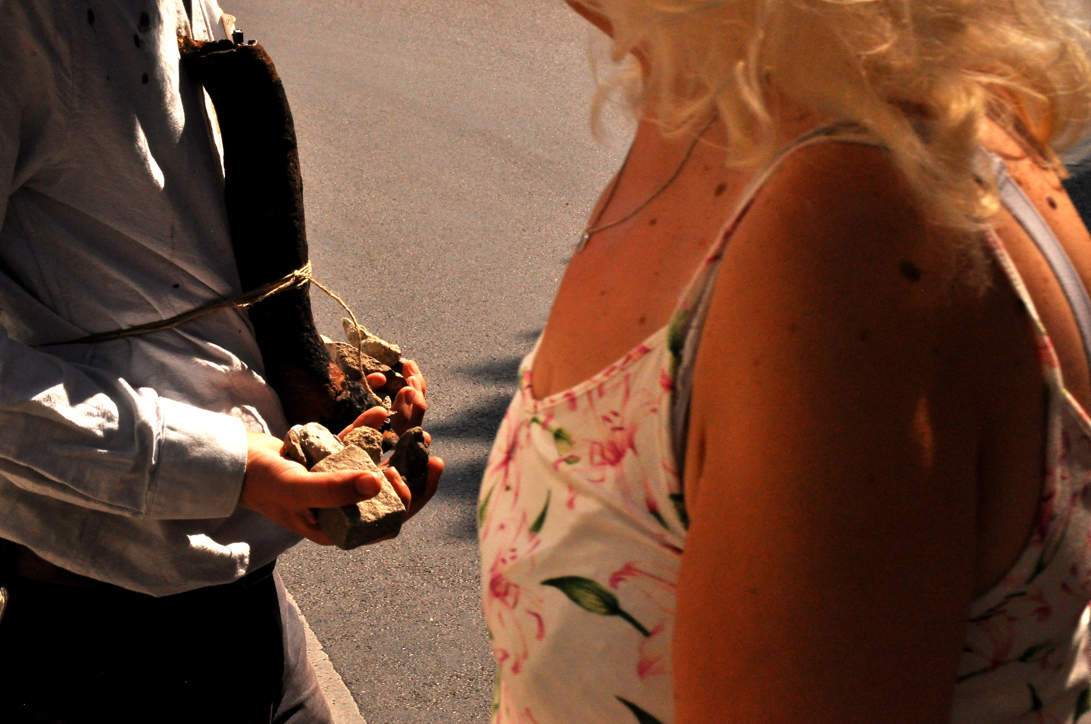 two people pass each other. you can only see their torsos. One is wearing a floral dress, one is holding small stones.