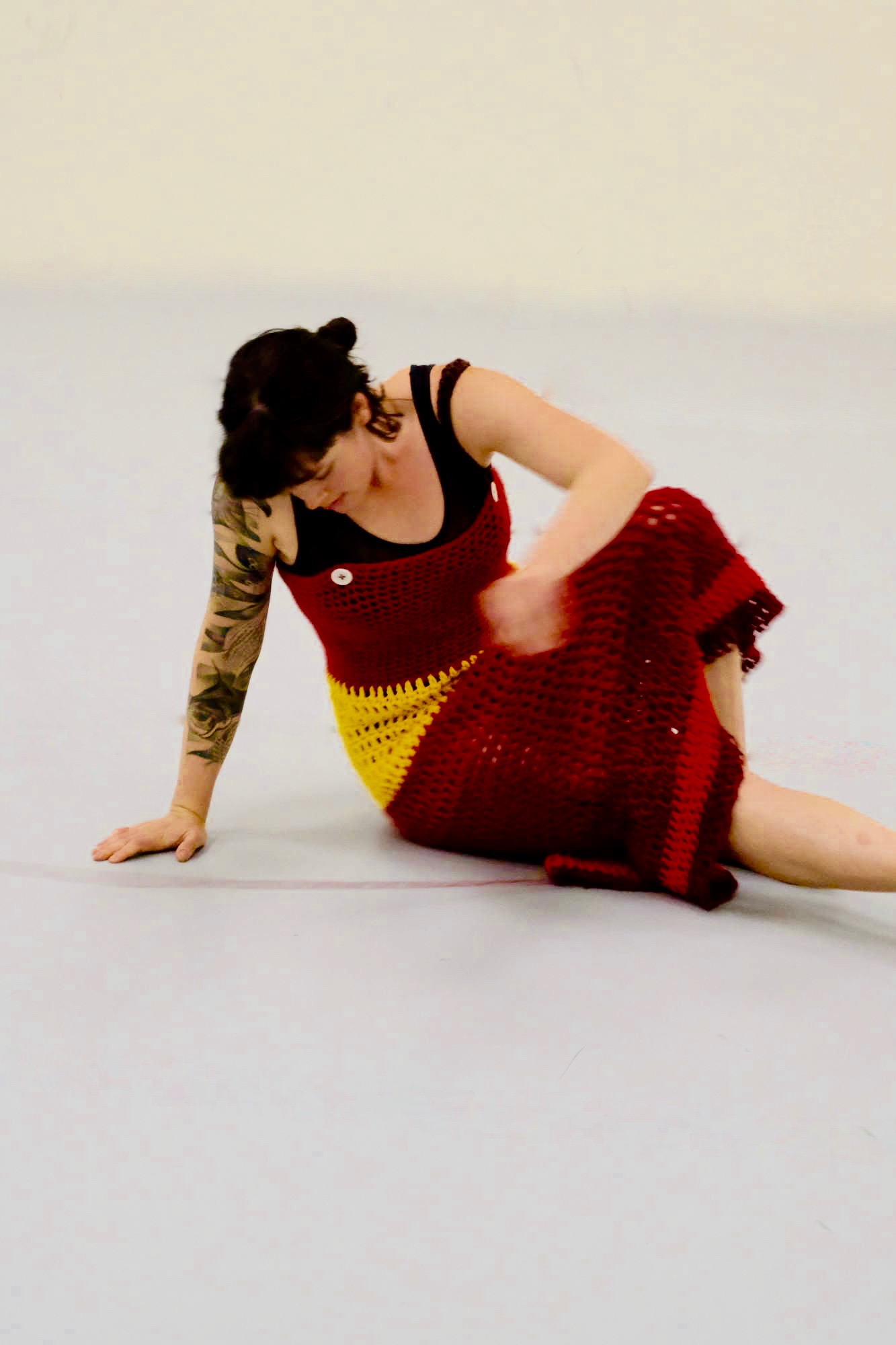 a dancer seated on the floor in a knitted dress leans on one arm and looks down