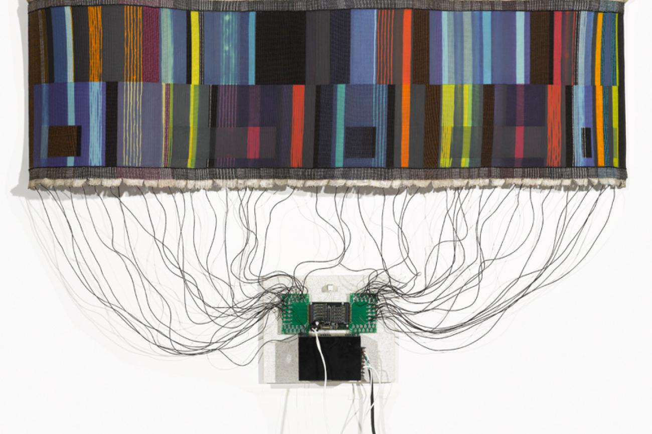 a textile weaving connected by dozens of wires to a microprocessor board