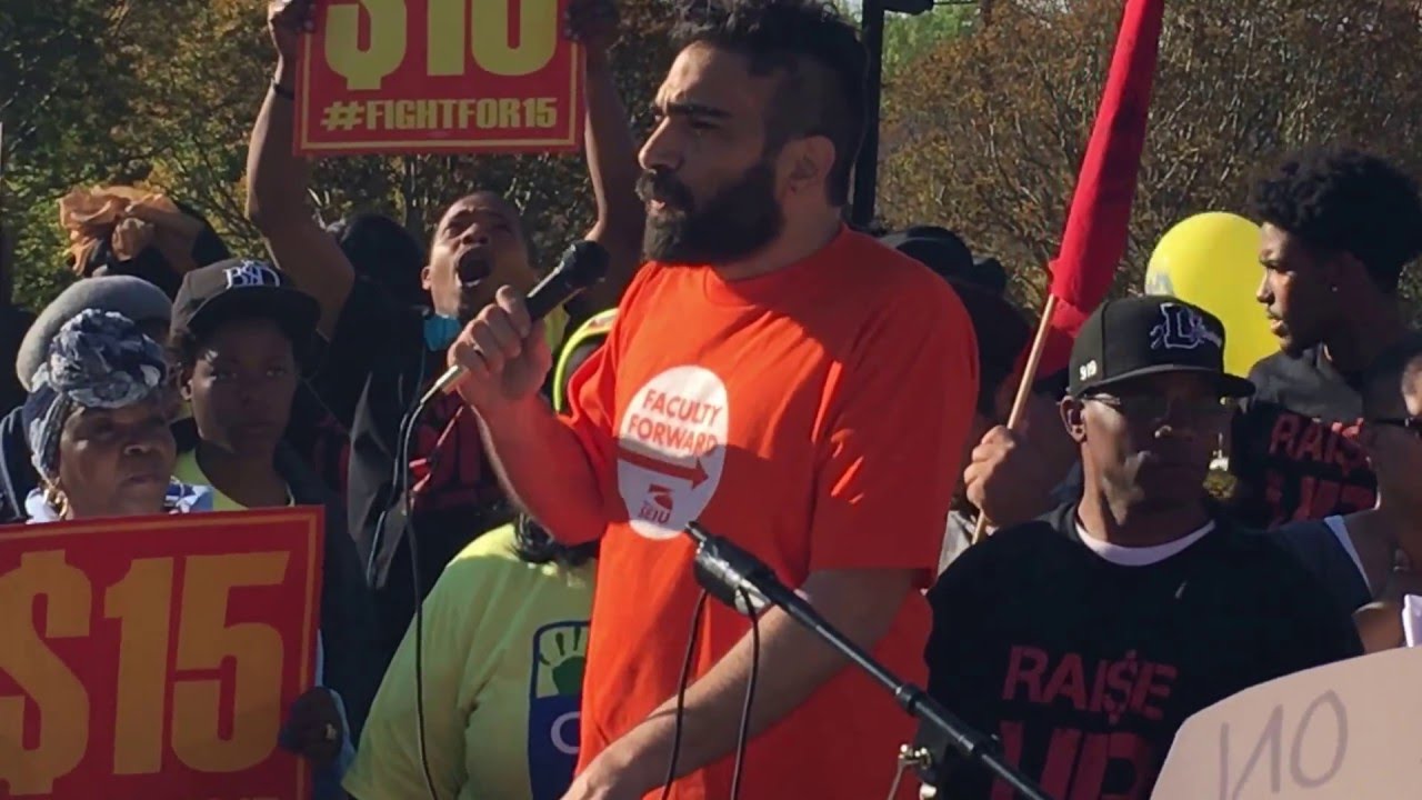 Dr. Peter Pihos wearing a faculty union t-shirt, speaking with microphone at a public demonstration