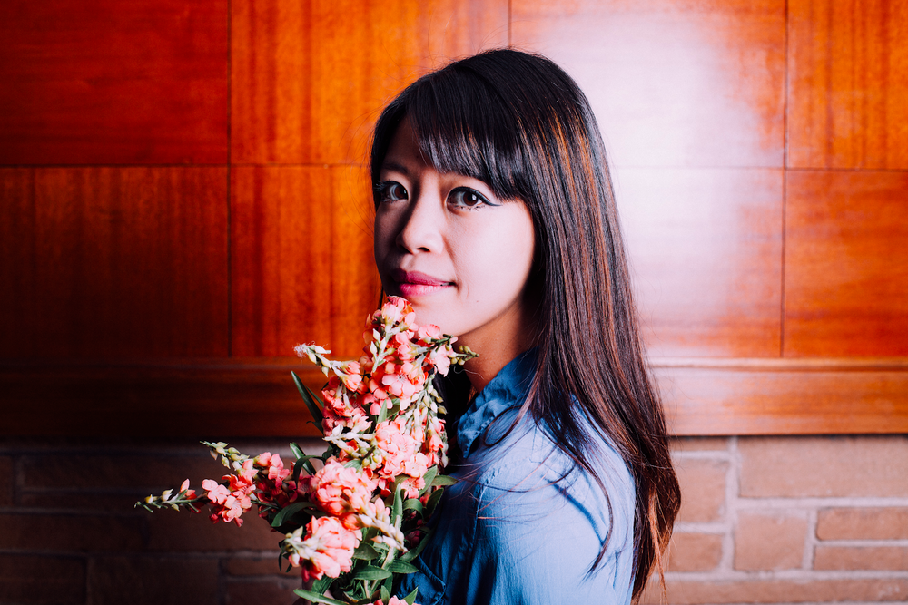 Jane Wong looks over her shoulder and holds a bunch of pink flowers near her chin.