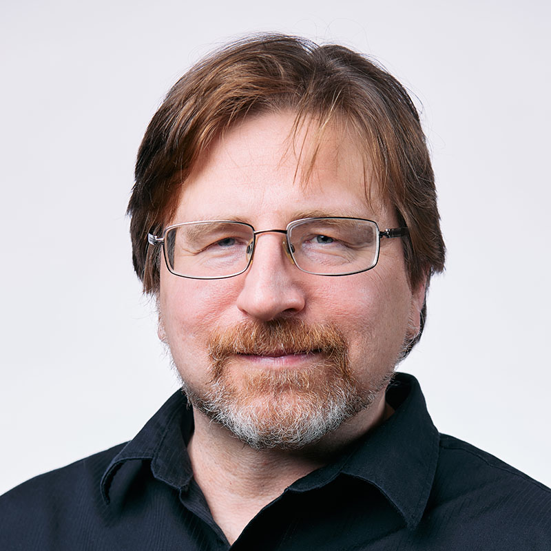 bearded fellow with straight brown hair, glasses, black collared shirt