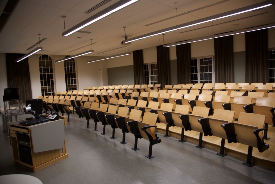 A room filled with rows of installed, folding chairs and a podium