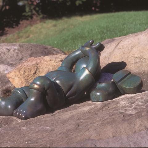 Tom Otterness sculpture Feats of Strength. A character stretched on a rock in a sunbathing pose. Full description in body text.