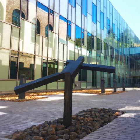 hominid form with rectangular limbs in a headlong run away from the view. Building with mirrored glass in background.