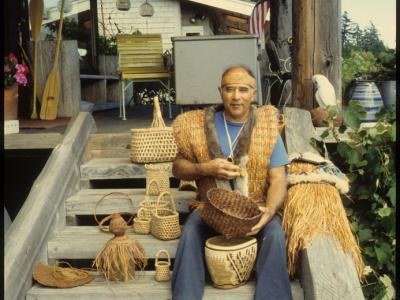 master weaver sitting on porch steps holding and surrounded by woven baskets