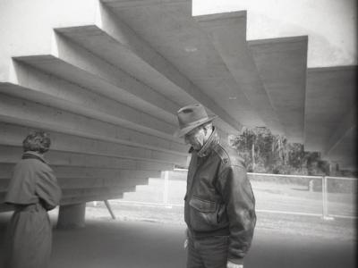 Two elderly people look downward as they walk below an arch of the Stadium Piece outdoor sculpture. The arch follows the same stair shape as the stairs above.