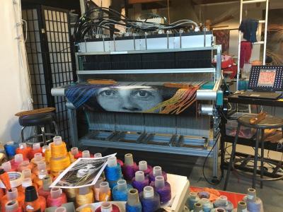 a giant loom or printer divulging fabric with a face on it. Pots of dye in the foreground.