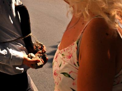 two people pass each other. you can only see their torsos. One is wearing a floral dress, one is holding small stones.