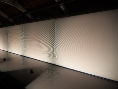 a shallow pool rippled by sound waves bounces reflected light onto a long blank wall