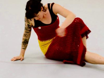 a dancer seated on the floor in a knitted dress leans on one arm and looks down