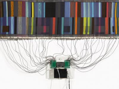 a textile weaving connected by dozens of wires to a microprocessor board