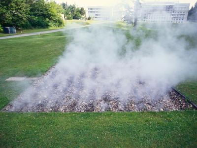 a large square of round stones in a grassy lacuna emits clouds of steam