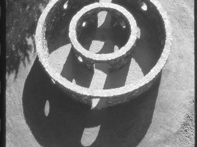arial view of two concentric rings of masonry. angled light reveals shadows of circular openings on the ground adjacent. Black and white photo.