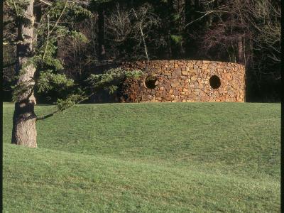 a curving masonry enclosure with round portals sits atop a grassy knoll