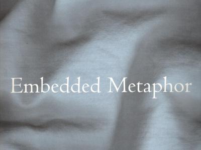 gently lit rumpled ivory fabric in soft folds with white letters: "Embedded Metaphor"
