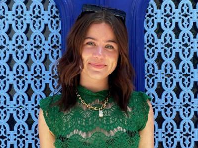 a smiling person in a textured green blouse in front of a deep blue textured screen window