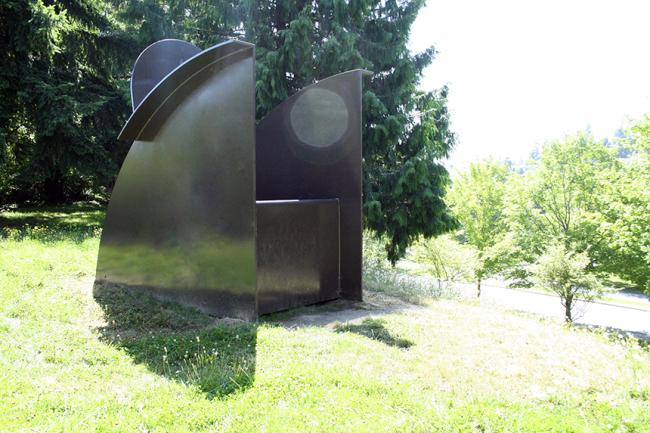 Large metal abstract sculpture resembling a chair sits on a grassy hill